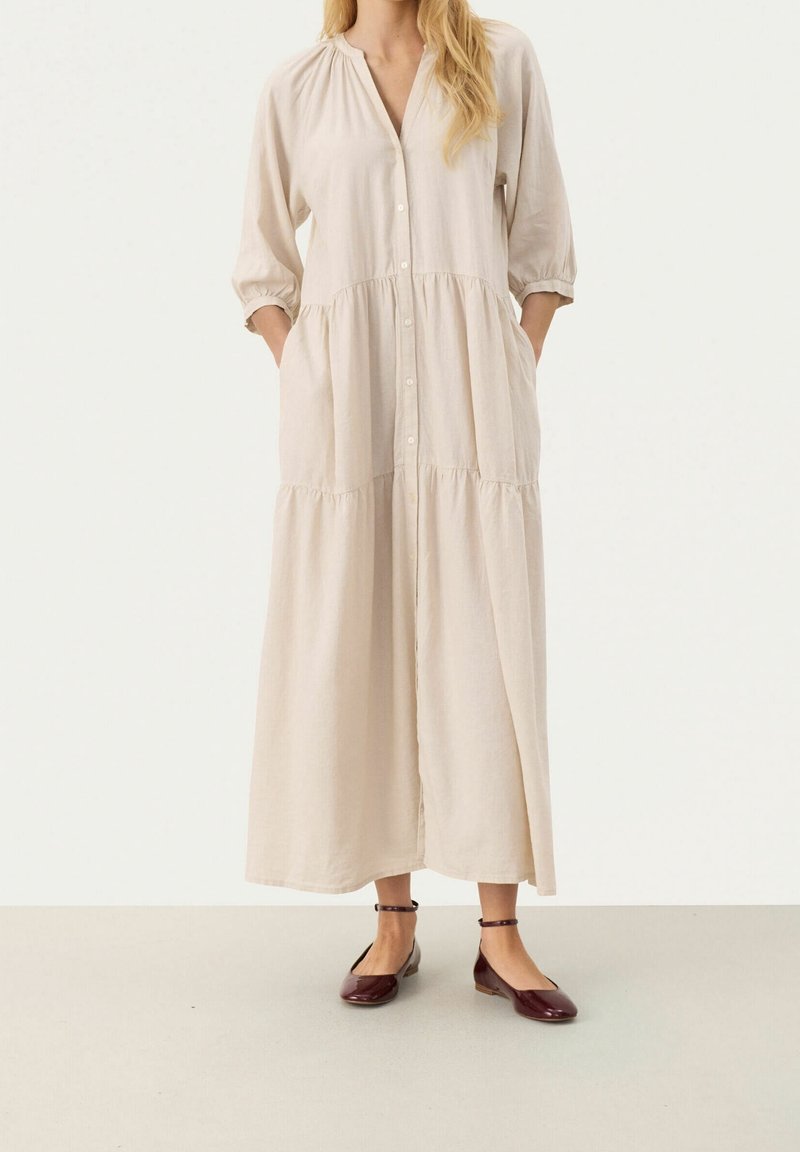 Robe en coton beige avec manches trois-quarts, devant boutonné, design à volants, poches latérales et coupe ample. Associée à des ballerines bordeaux.