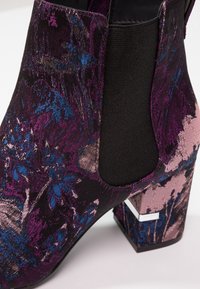 Bottine à talon bloc avec motif floral abstrait multicolore dans des tons violet, bleu et rose avec un panneau latéral élastique noir.