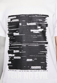 Hvid bomulds T-shirt med et dristigt sort grafisk design med gennemstreget tekst og sætningen "FEAR NO EVIL" i bunden.