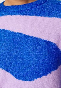 Närbild av en stickad tröja med djärva diagonala ränder i blå och lavendelfärger.