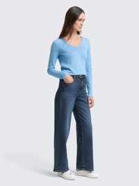 Lichtblauwe, lange mouwen gebreide trui met een V-hals, gecombineerd met donkerblauwe wide-leg jeans en witte sneakers. Soepele textuur, casual pasvorm.