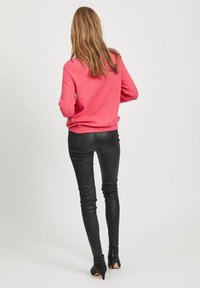 Roze pulover s dugim rukavima i rebrastim rubom, uparen s crnim kožnim prilagođenim hlačama i čizmama na visoku petu, prikazan iz pozadine.
