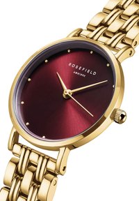 Montre-bracelet dorée avec un cadran bordeaux. Présente des marqueurs horaires minimalistes et un bracelet en or au design texturé. Mouvement à quartz.