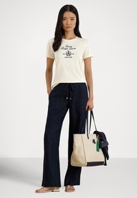 Ανοιχτόχρωμο κρεμ t-shirt με ναυτικό λογότυπο, συνδυασμένο με φαρδιά ναυτικά παντελόνια. Μεγάλη μπεζ τσάντα ώμου με σκούρες λεπτομέρειες και πράσινη φούντα.