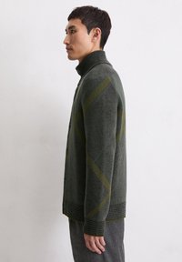 Green knitted cardigan with a high collar, featuring a diamond pattern in darker green and yellow accents, buttoned with ribbed cuffs and hem.