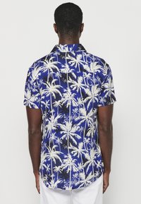 Camicia a maniche corte in tessuto blu con un motivo di palme bianche e nere, con colletto e orlo curvo.