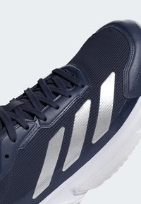 Granatowe buty sportowe z teksturowanej tkaniny, srebrnym logo w trzy paseczki i białą podeszwą. Wyposażone w płaskie sznurówki i wyściełany kołnierz.