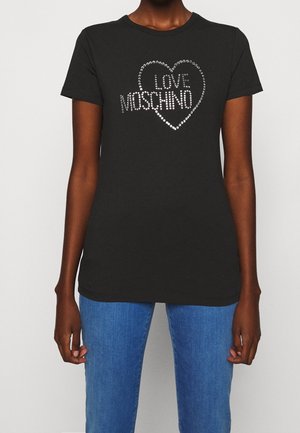 Zwart T-shirt met korte mouwen met een zilveren gestikte hart en de tekst "LOVE MOSCHINO" gedragen door een persoon in blauwe jeans tegen een effen achtergrond.