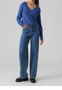 Maglione blu lavorato a maglia con scollo a V, abbinato a jeans di denim a vita alta e gamba larga e scarpe platform nere.