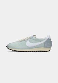 Svijetloplavi niskotop s tenisicama s bijelim Nike znakom, kremastim vezicama, bež potplatima i crnim teksturiranim potplatom prikazan sa strane.