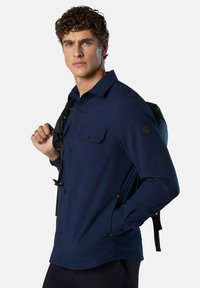 Marineblaue Knopfjacke aus leichtem Stoff. Sie verfügt über zwei Brusttaschen, einen lockeren Schnitt und ein Etikett am Ärmel.