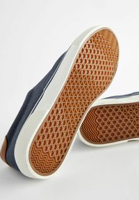 Donkerblauwe canvas sneakers met witte rubberen zolen, voorzien van een hexagonaal patroon in de bruine buitenzool en leren accenten rond de hak.