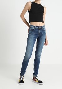 Wąskie niebieskie dżinsy z efektem sprania i przednimi kieszeniami, zestawione z czarnym topem bez rękawów i wielokolorowymi sneakersami.