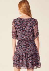 Blumenkleid mit kurzen Ärmeln, tailliertem Schnitt und ausgestelltem Rock. Der Stoff ist leicht und halbtransparent mit einem dunklen Hintergrund.