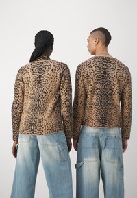 Luipaardprint trui in bruin en zwart, met lange mouwen en ronde hals, gecombineerd met lichtblauwe wijde jeans. Gestructureerd breisel design.