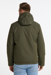 Jachetă cu capotă de culoare verde măslinie, cu un exterior neted și rezistent la apă, talie elastică și cusături simple. Afișată din spate, purtată cu blugi de culoare albastră deschisă.