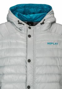 Silberne Pufferjacke mit türkisfarbenem Innenfutter der Kapuze. Ausstattung mit einem Reißverschluss und Knopfverschluss sowie dem blauen "REPLAY"-Logo auf der Vorderseite.