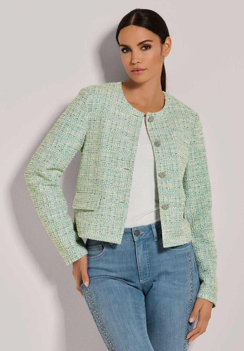 Mintgrünes Tweed-Jacket mit Rundhalsausschnitt, Fronttaschen und dekorativen silbernen Knöpfen, kombiniert mit hellblauen Jeans mit Nietenakzenten.
