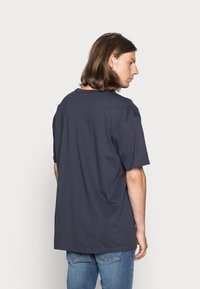 Tricou scurt cu mânecă scurtă de culoare albastru închis, cu guler rotund, fabricat din bumbac, având o croială lejeră și detalii de cusătură vizibile.
