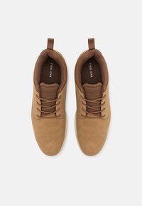 Baskets en daim marron avec un bout rond, un laçage à l'avant et une languette; elles présentent une semelle en caoutchouc blanche contrastante et un intérieur texturé.