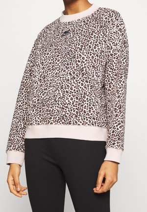 Femme portant un sweat-shirt Nike à manches longues en imprimé léopard avec des poignets et un ourlet rose clair, associé à un pantalon noir.