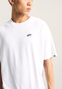 White cotton t-shirt featuring a small black "Off the Wall" logo on the left chest. The shirt has a round neckline and short sleeves.