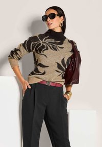 Frau trägt einen beigen Pullover mit schwarzen Blumenmustern, schwarze Hosen mit einem roten Gürtel, große goldene Creolen, schwarze Sonnenbrille und eine kastanienbraune Schultertasche.