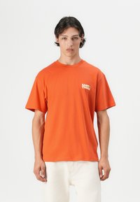 Oranje katoenen T-shirt met korte mouwen en een ronde hals. Voorzien van een klein wit "SAINT-TROPEZ" tekstlogo op de linkerborst.
