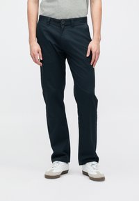 Σκούρο μπλε παντελόνι σε ίσια γραμμή με λεία υφή. Διαθέτει κλείσιμο με κουμπιά και πλαϊνές τσέπες, και συνδυάζεται με λευκά αθλητικά παπούτσια.