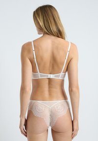 Set di lingerie bianco in pizzo che presenta un bralette trasparente con spalline regolabili e una schiena decorativa, abbinato a delicate mutandine in pizzo.