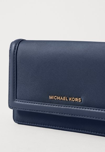 Portefeuille en satin bleu marine avec une texture lisse, arborant un logo "MICHAEL KORS" en ton doré. Design élégant et rectangulaire avec des détails de couture.