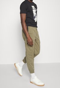 Svart grafisk t-shirt, olivgröna cargobyxor med elastiska mudd, vita sneakers och ankelsockor. Avslappnad outfit med funktionella fickor.