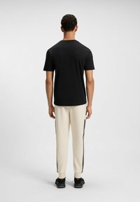 Black short-sleeve t-shirt paired with cream joggers featuring black side stripes and black athletic shoes, showing a back view.