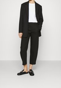 Zwarte op maat gemaakte blazer, witte T-shirt, zwarte cropped broek en zwarte instapschoenen met zilverkleurige hardware. Gladde stof en gestructureerd ontwerp.