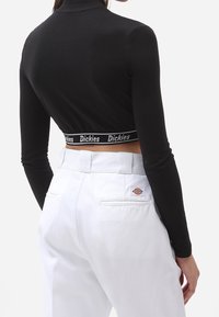 Mustat pitkät hiha crop-topit, joissa on korkea kaulus ja brändätty elastinen nauha helman kohdalla, yhdistettyinä valkoisiin housuihin, joissa on hienovarainen logo.