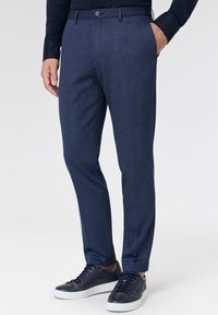 Donkerblauwe broek met een subtiel textuurpatroon, voorzien van zijzakken en een knoopsluiting, gecombineerd met donkere sneakers.