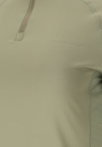 Close-up of beige athletic fabric with a textured side panel and subtle "ENDURANCE" logo near a vertical zipper.