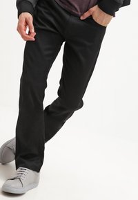 Pantalones negros de tejido liso con corte recto. Combinados con zapatillas grises claras. Diseño minimalista, sin patrones ni detalles visibles.