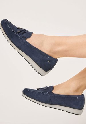 Navy suede moccasin shoes with a flat design, featuring a lace detail, rubber sole, and contrasting stitching along the edge.