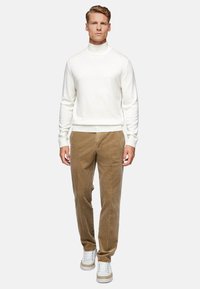 White turtleneck sweater, beige corduroy pants, and white sneakers with light beige accents. Textured materials and fitted design.