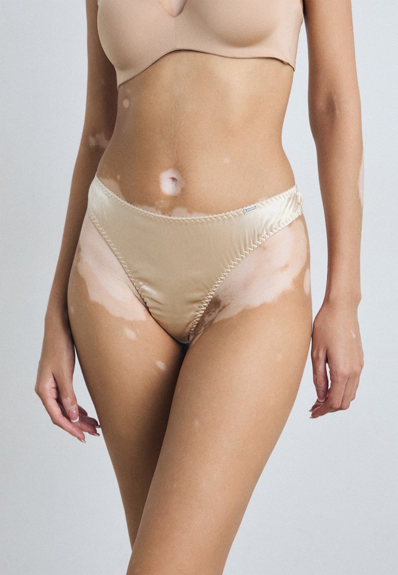 Bas de bikini satin nude avec un design hautement découpé. Texture lisse, coutures décoratives le long des bords et un minimalisme dans les détails.