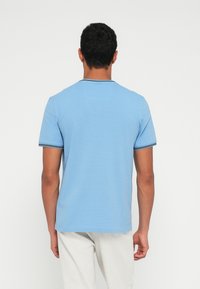 Jasnoniebieska koszulka z krótkim rękawem i okrągłym dekoltem, z czarno-białymi paskami na kołnierzyku i rękawach.