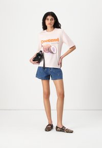Lichtroze t-shirt met "Coconut" graphic en illustratie, gecombineerd met blauwe denim shorts. Accessoires zijn een zwarte tas en schoenen met luipaardprint.