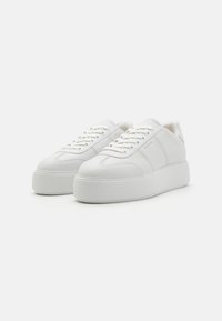 Hvite lær sneakers med en teksturert plattformsåle, flate lisser og minimalistisk design. Har subtile sømmer og merkevaredetaljer.