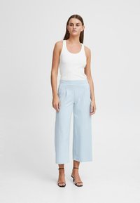 Lichtblauwe wijde broek met plooien, gemaakt van zacht materiaal. Gecombineerd met een aansluitend wit geribd hemdje en zwarte strap sandalen.