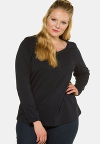 Mustapaita, jossa on pitkät hihat ja avara pääntie, etuosassa nappirivi. Pehmeä kangas, jossa rento istuvuus.