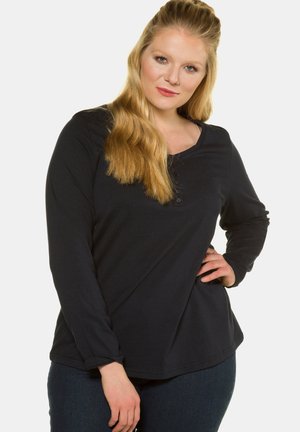 Maglietta nera a maniche lunghe con scollatura a barca, caratterizzata da una fila di bottoni lungo la parte anteriore. Tessuto morbido con vestibilità comoda.