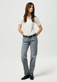 Camisa polo blanca de ribete con mangas cortas y tapeta de botones, combinada con jeans de pierna recta azul claro y un cinturón negro. Botas negras de punta afilada.