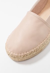 Espadrille de cuero rosa claro con suela de yute trenzado, punta redondeada y acentos cosidos a lo largo del borde. Diseño simple y minimalista.