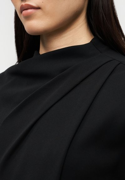 Μαύρο φόρεμα με λεπτομέρεια ραμμένης ύφανσης, διαθέτει απαλό υλικό και πιέτες γύρω από το λαιμό, δημιουργώντας ένα ομαλό περίγραμμα.